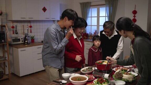 穿着红色衣服的兴高采烈的亚洲老年母亲和儿子说话儿媳在餐桌上用筷子准备火锅在准备年夜饭