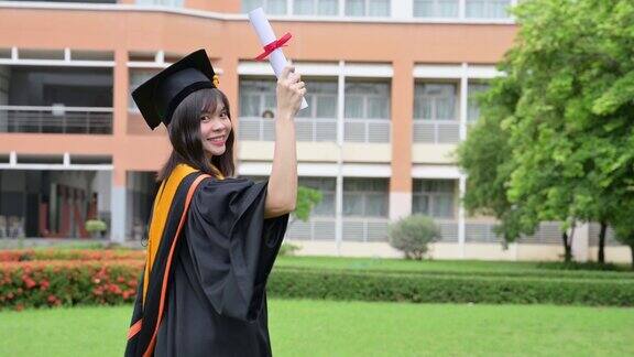 亚洲女毕业生身穿黑色长袍头戴金色流苏的黑色帽子拿着文凭微笑着祝贺大学