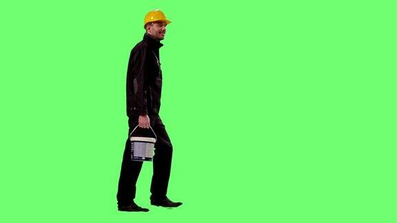 建筑工人戴着安全帽背着油漆桶在绿色屏幕上行走
