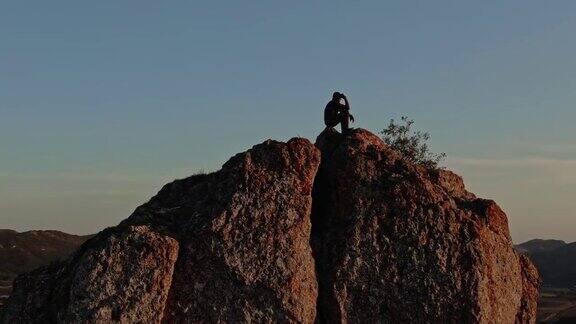 一个人坐在山顶上被夕阳的最后余晖照亮鸟瞰图测量由无人驾驶飞机