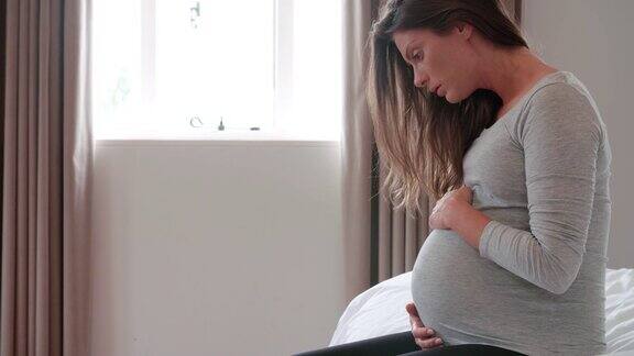 沮丧的孕妇抱着肚子坐在床上