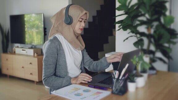 穆斯林妇女在家里的客厅用笔记本电脑工作