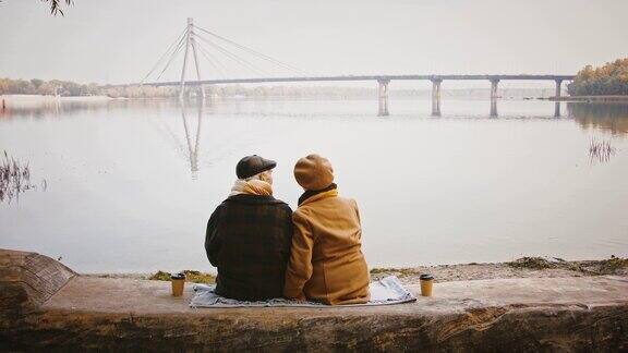 秋日老夫老妻们坐在河边的长凳上谈笑风生望着桥上的风景