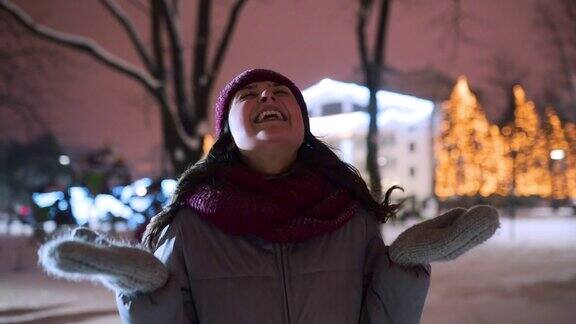 在圣诞市场的冬夜年轻女子在户外享受飘落的雪花快乐的女孩在雪花下在公园里张开双臂用手、嘴去接雪花女性向天空伸出双臂