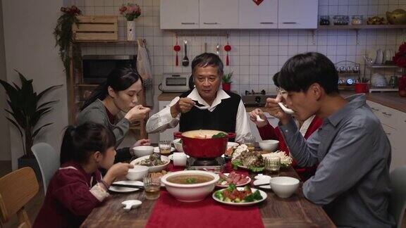 亚洲的大家庭在晚上聚在一起吃团圆饭的时候用勺子吹和品尝热腾腾的美味汤