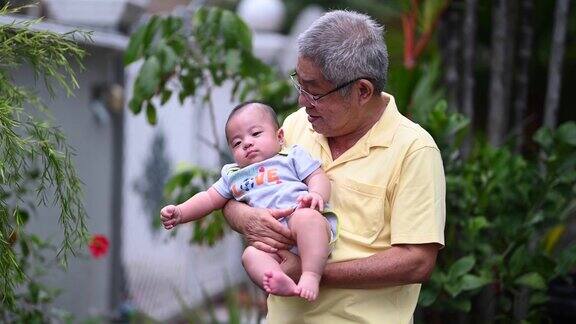 一位亚洲华人老人抱着他的小孙子站在他们家的前院