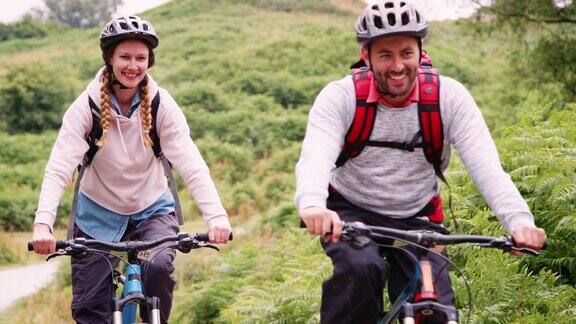 年轻的成年夫妇在乡村露营度假期间湖区英国骑山地自行车