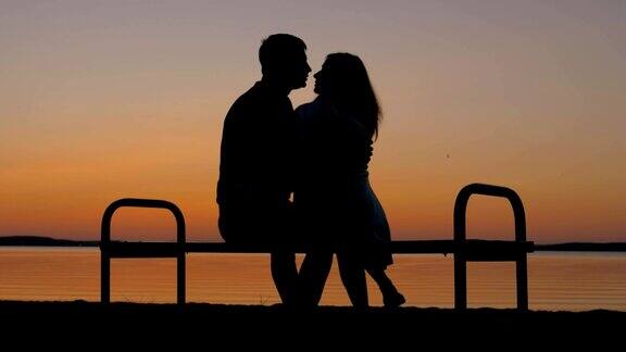 一对情侣坐在长椅上拥抱在沙滩上欣赏日落