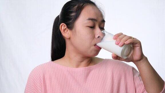 快乐的女人喝着杯子里的牛奶在工作室的白色背景上竖起大拇指健康的营养
