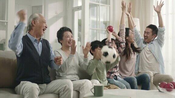 三代亚洲家庭在家里看电视直播的足球比赛