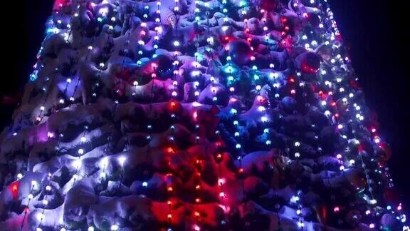 在下雪的冬夜城市广场上挂着发光的花环和装饰的大圣诞树特写镜头室外装饰的新年树相机倾斜了