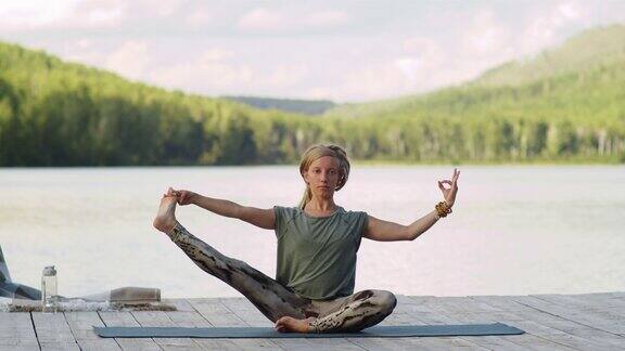 在湖边的木码头上做瑜伽伸展腿的女人