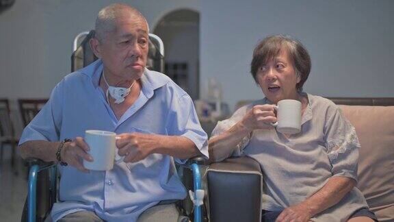 亚洲华人老夫妇坐在轮椅上享受电影之夜坐在客厅的沙发上看电视