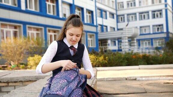 少女坐在学院的院子里在他的背包里找东西