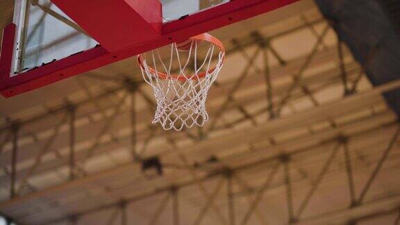 在玻璃篮板上飞向篮筐的篮球投球击中环和网从下面看