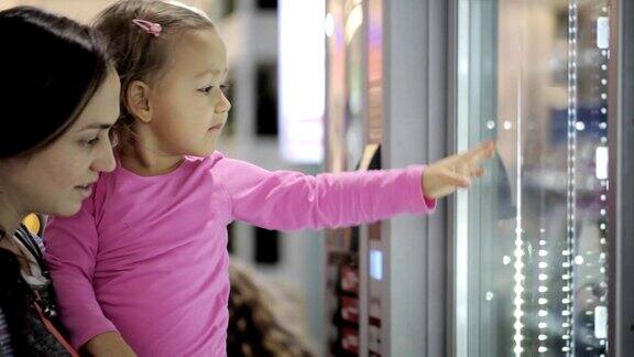 母亲和女儿在机场内的自动售货机选择零食