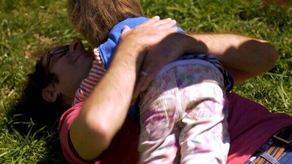 两个年幼的孩子在草地上摔跤拥抱着他们的父亲