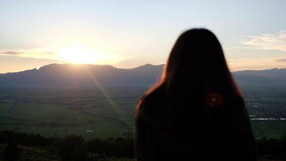 一个女人在傍晚看日落和山景的慢动作后视镜