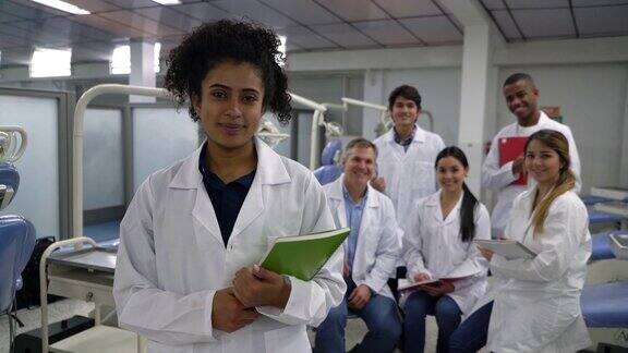 美丽的黑人牙科学生和她的同学和老师在背景都对着镜头微笑