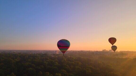无人机观看彩色的热气球飞过绿色公园和河流在小欧洲城市在夏天日出