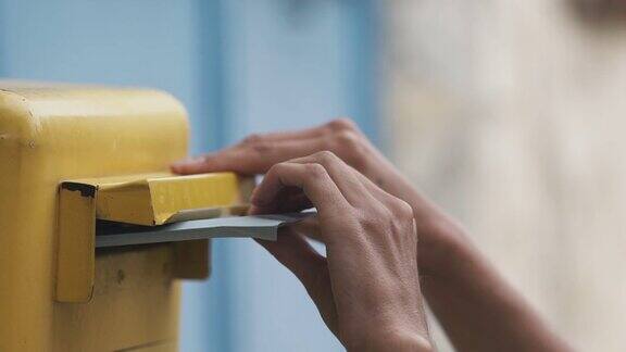一位女士正在把一封蓝色的信投进一个黄色的信箱
