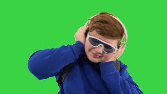 男孩戴着时髦的太阳镜戴着耳机在绿屏上听音乐