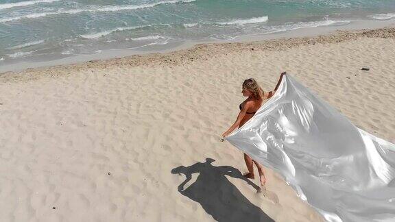一个女人在海滩上拿着白色的摇动的织物