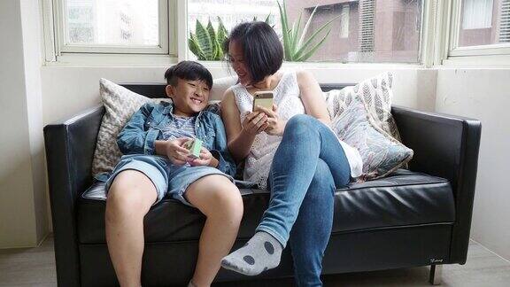 母亲和儿子一起用手机坐在家里的沙发上