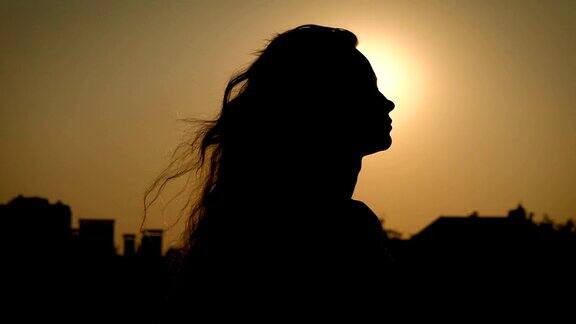 侧面的黑色剪影的女人摆姿势在散射的日落光在农村背景