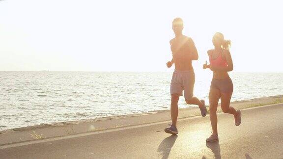 慢镜头:运动的女人和男人度假时在美丽的海边跑步