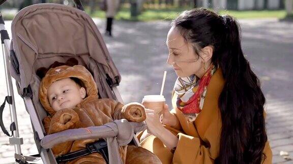 妈妈在公园里微笑着跟婴儿车里的孩子说话