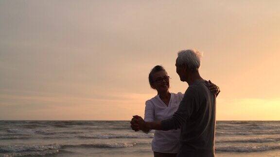 亚洲夫妇老年人退休休息放松跳舞日落海滩蜜月家庭一起幸福的人生活方式慢镜头