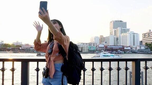 亚洲女游客用智能手机自拍并挥手
