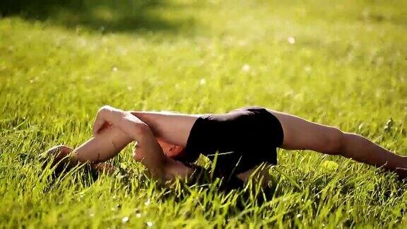 娇小柔韧的女孩在草地上做复杂的体操动作