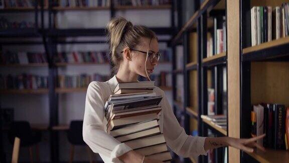 一个金发女人在图书馆里拿着一堆书把更多的书放在书架上