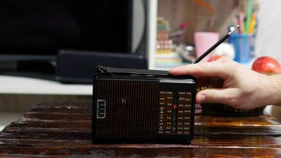 在一张旧木桌上收音机里播放着无线电波带天线的古董接收机的生活方式把模拟收音机调到一个音阶上一个男人在用一台旧收音机听新闻听音乐