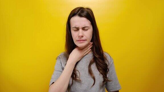 不幸生病的年轻女子喉咙痛生病和不舒服遭受喉咙痛感冒后感到疼痛穿着灰色t恤站在黄色的背景疾病引起的不适