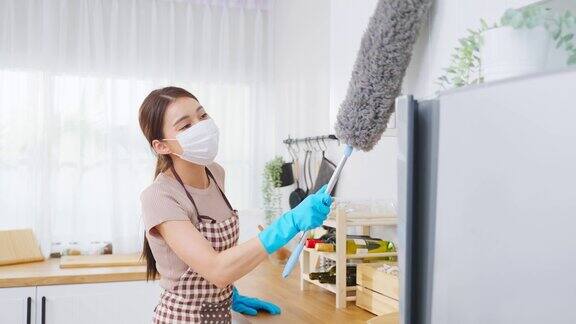 亚洲清洁服务女工清洁厨房和漂亮的女管家清洁工戴着口罩用鸡毛掸子擦拭凌乱的柜台为管家做家务或杂务