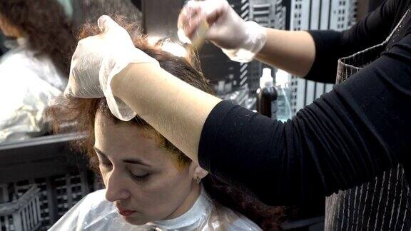 特写理发师在理发店里画了一个东方女孩的头发然后用刷子把颜料涂在她的头上头发护理4k25fps