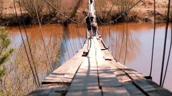 年轻的家庭妈妈、爸爸和女儿走在河上的老吊桥上