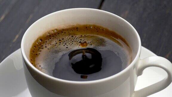 一滴一滴的咖啡掉进了浓缩咖啡杯黑色木制背景慢动作镜头