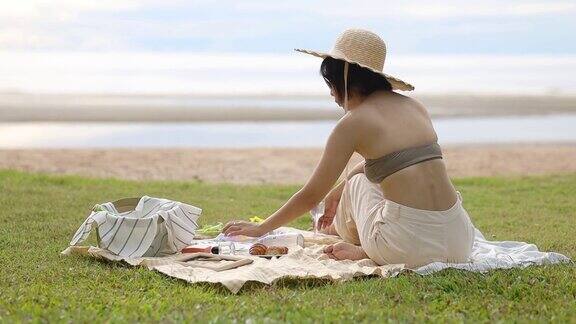 快乐的年轻女人坐在海边与野餐的东西一起冷却