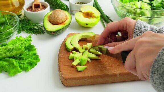 一位妇女正在用新鲜的绿色蔬菜和香草做沙拉生食素食菜单烹饪健康饮食或素食女人们用手在菜板上切牛油果周围是绿色的蔬菜循序渐进食谱