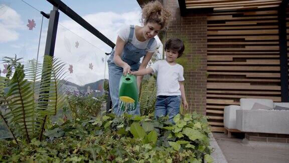 快乐的拉丁美洲母亲教她的儿子如何在他们家的花园浇水