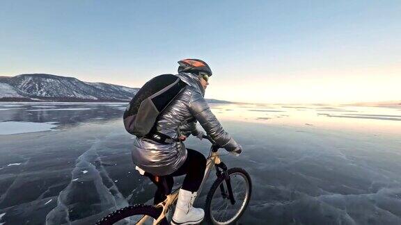 一个女人在冰上骑自行车这个女孩穿着银色的羽绒服背着自行车背包戴着头盔结冰的贝加尔湖的冰自行车的轮胎上覆盖着特殊的尖钉