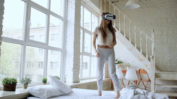 快乐微笑的年轻女子跳舞同时获得体验使用360VR头盔眼镜的虚拟现实在家床上