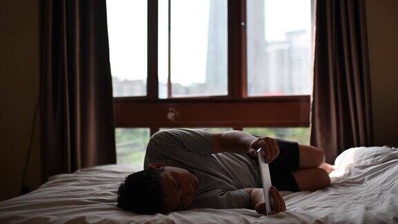 一个亚洲中年人中午躺在卧室的床上用他的笔记本电脑上网