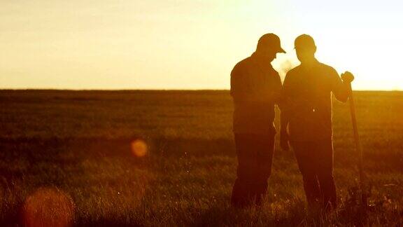 两个农民在地里聊天用着药片美丽的夕阳两个男人的剪影Copyspace组成