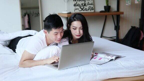 亚洲华人夫妇拥抱在床上用手提电脑上网在早上