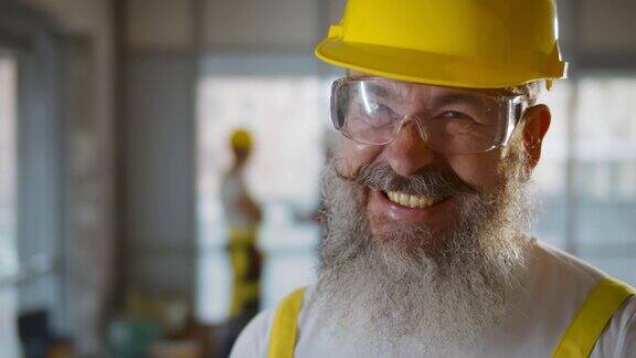 留着胡子的高级建筑工人戴着建筑头盔和塑料眼镜的肖像